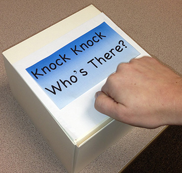Hand knocking on White box with Knock Knock Whose There written on it