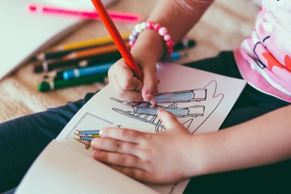 child drawing on paper with colored pencils