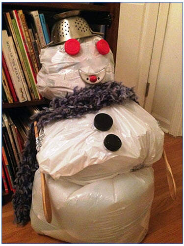 Snowman made from white trash bags wearing a strainer hat and scarf