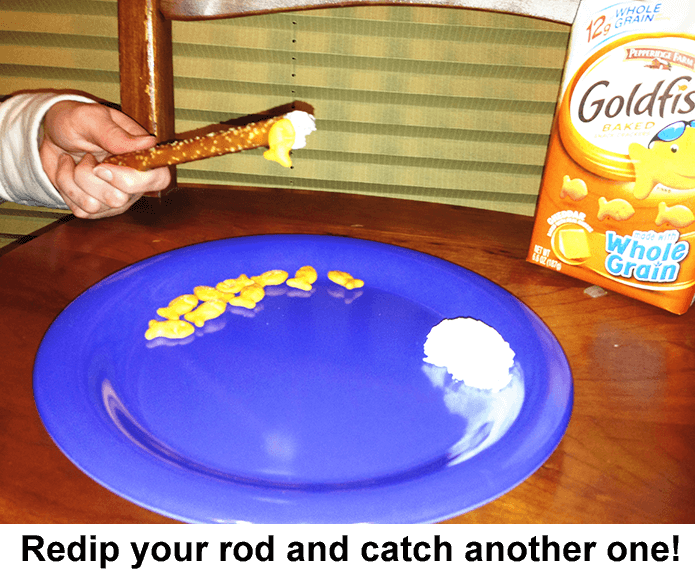 Hand using a pretzel rod with cream cheese on end to pick up goldfish crackers