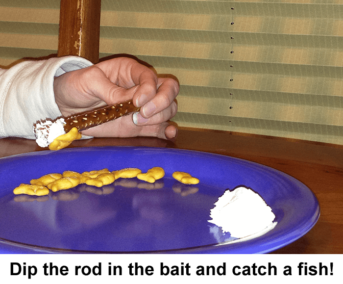 Hand using a pretzel rod with cream cheese on end to pick up goldfish crackers