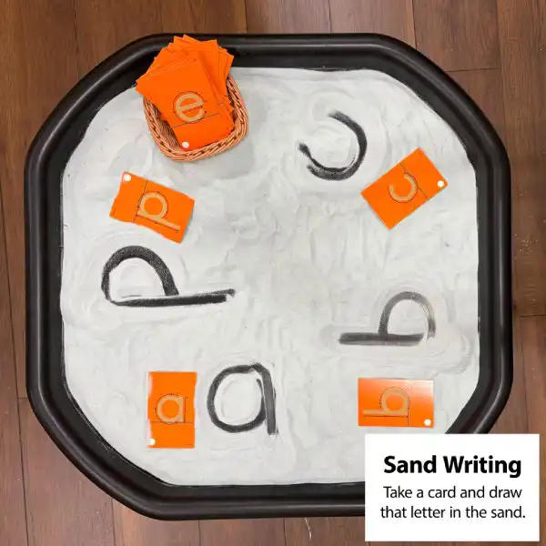 Literacy tuff tray activity with sand and tactile letters for preschool writing practice.