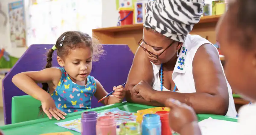 ​​Teacher sitting with child creating art with paint​