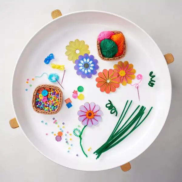 Fine motor tuff tray activity using flowers, beads, and yarn for threading practice.