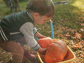 Toddler boy lifting orange pumpkin