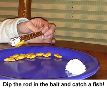 Hand using a pretzel rod with cream cheese on end to pick up goldfish crackers