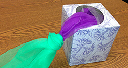 Square tissue box with a green and purple scarf coming out the top