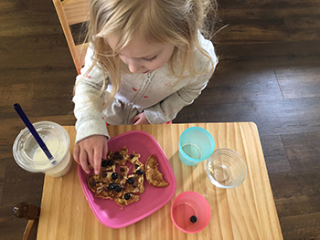 child sitting at table with plate of food