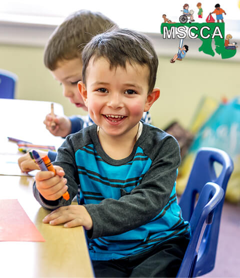 Preschool child sitting at table holding crayons in Maryland State Child Care Association classroom