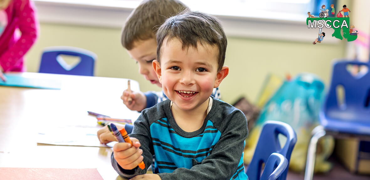 Preschool child sitting at table holding crayons in Maryland State Child Care Association classroom